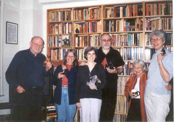 a group of people smiling at the camera and hugging each other, against a backdrop of book stacks